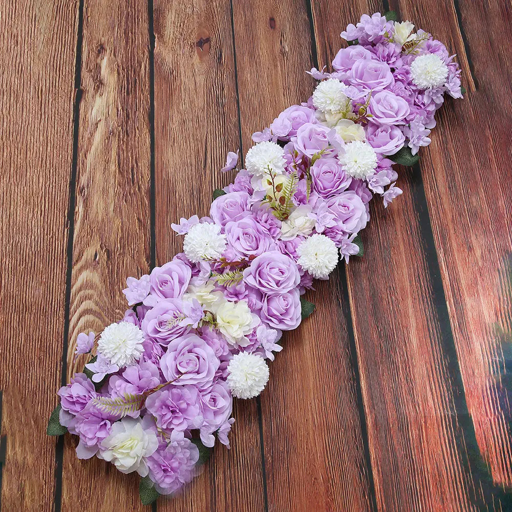Composition de fleurs de sol pour mariage de rose blanche, présentant une guirlande florale décorative avec des roses artificielles lavande et blanches, accompagnée de pompons blancs duveteux et de verdure.