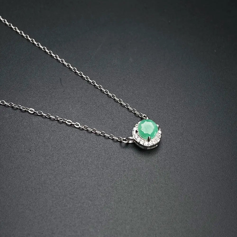 A delicate sterling silver chain necklace with a central round emerald stone surrounded by a halo of small diamonds in an emerald sterling silver jewelry set.