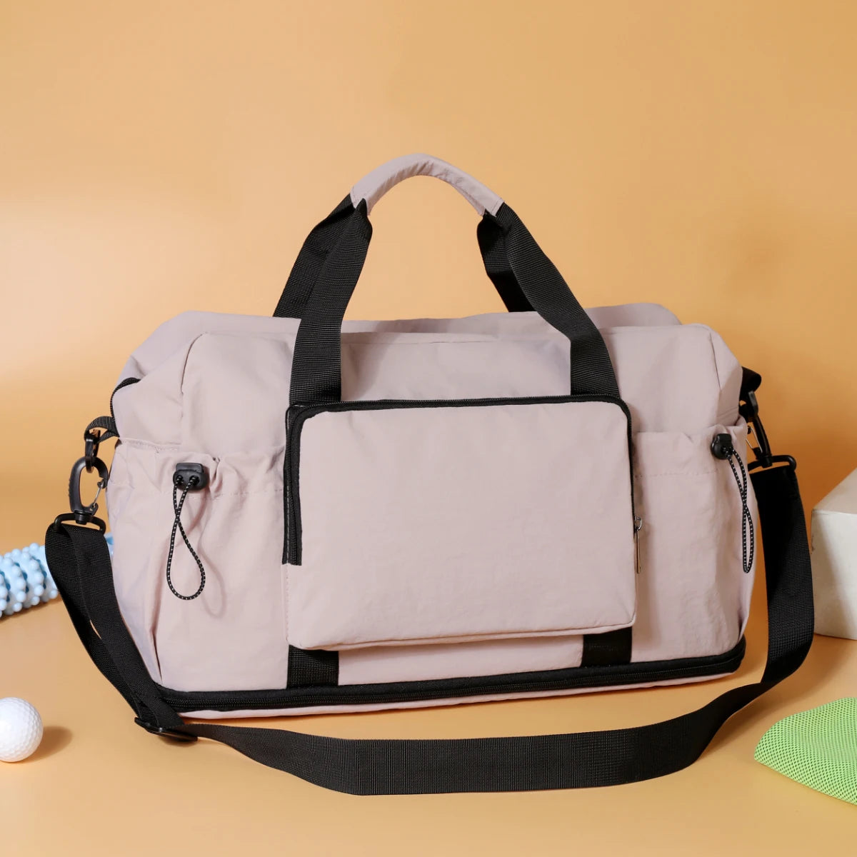 Sac de sport duffel beige avec poignées et bandoulière en tissu noir, doté de plusieurs compartiments zippés pour une bagagerie de voyage légère extensible.