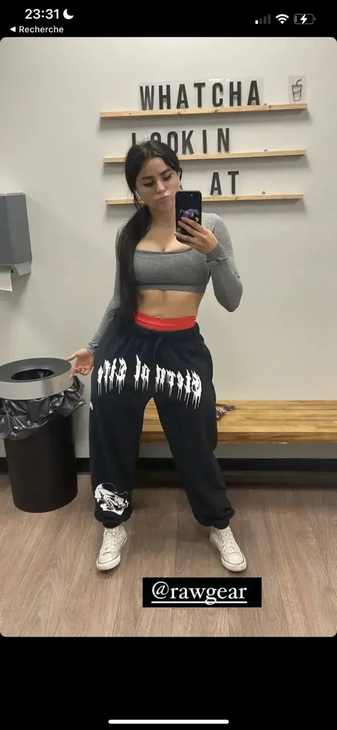 Pantalons d’entraînement graphiques pour hommes, sweatpants noirs, avec des lettres blanches de style graffiti et un écusson graphique sur la cheville gauche, conçu pour un usage en vêtements d’entraînement.