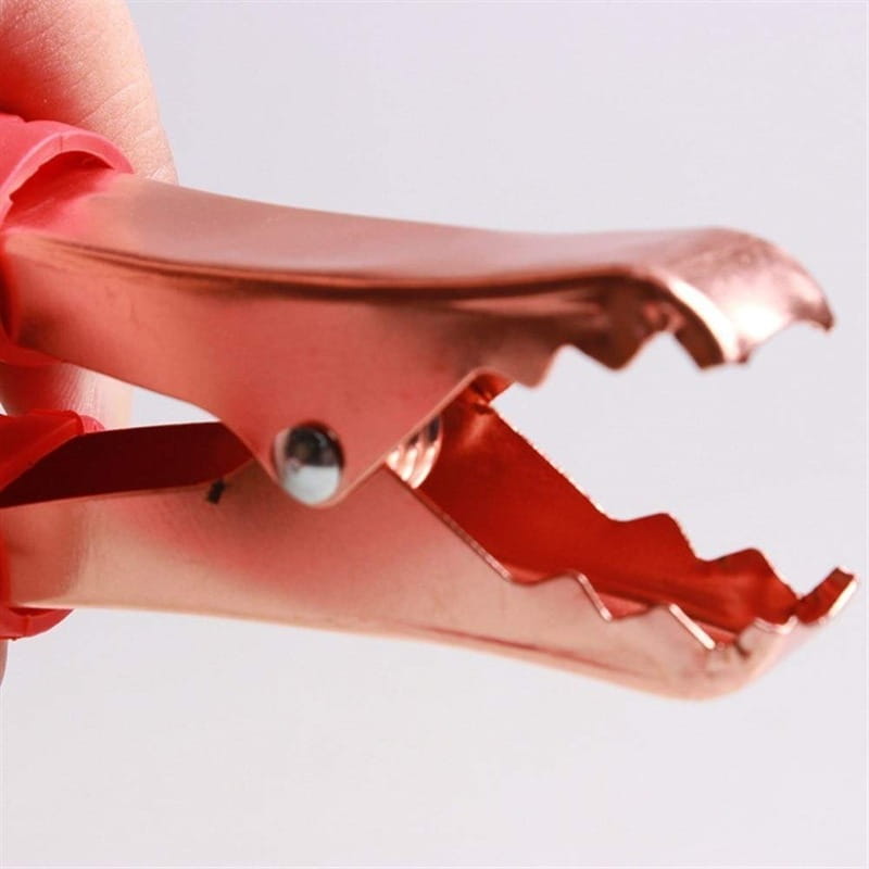 Câbles de démarrage pour voiture en métal de couleur or rosé 500 A, pinces pour batterie avec mors crantés et une poignée isolée rouge.