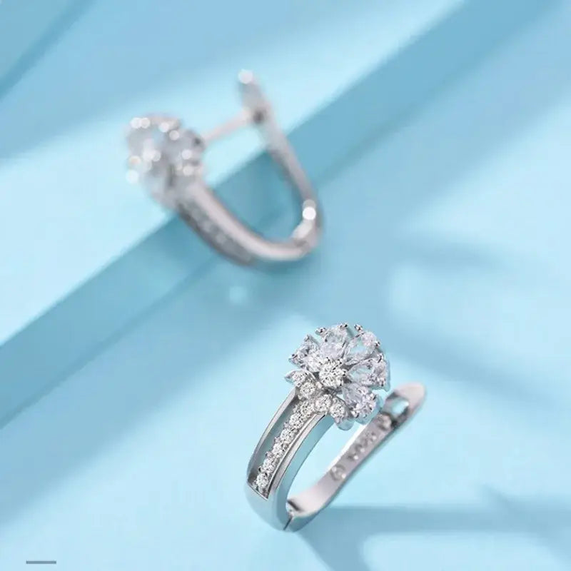 Pendientes de flores de circonio en plata de ley con un pendiente plateado brillante que presenta un conjunto de cristales claros dispuestos en un patrón floral y acentuado por piedras más pequeñas a lo largo de la banda.