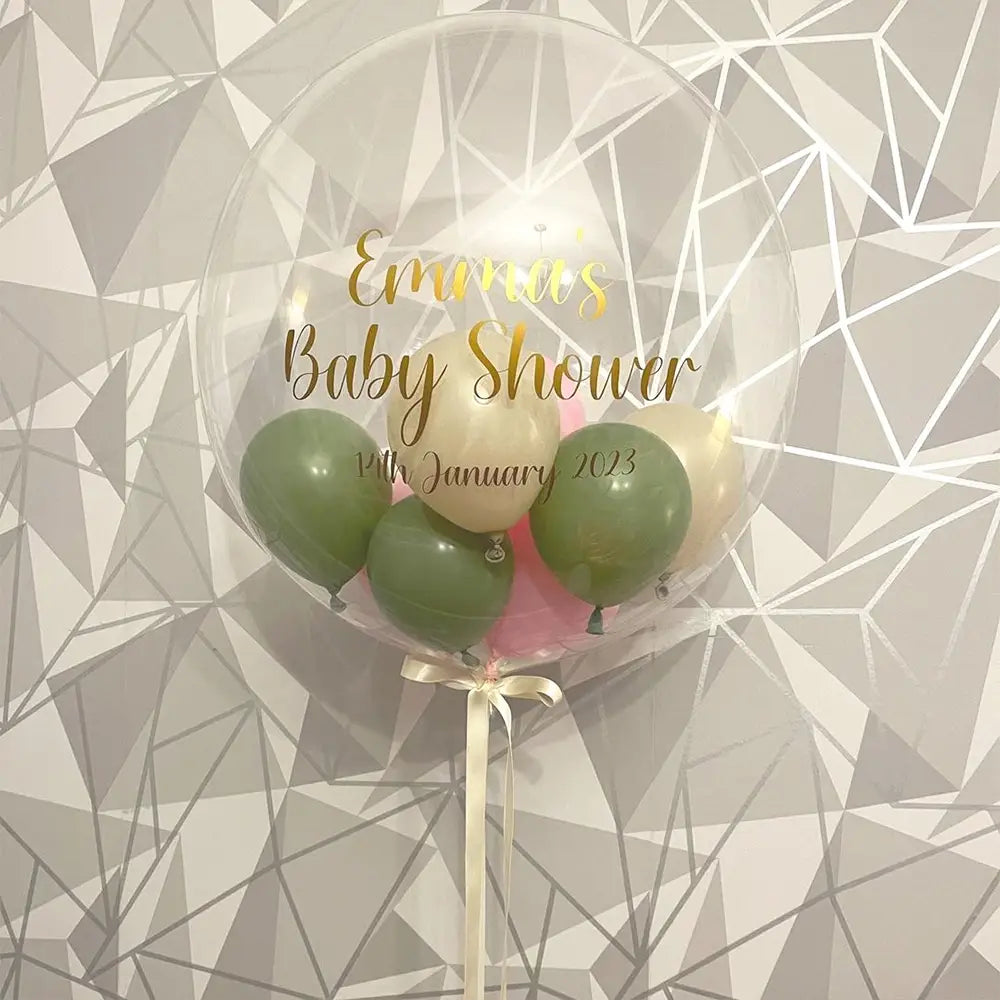 Klarer transparenter 36-Zoll-Bobo-Ballon mit goldfarbener Folien-Baby-Party-Aufkleber-Beschriftung „Emma’s Baby Shower 14th January 2023“, enthaltend grüne, cremige und rosafarbene Ballons, gebunden mit einer weißen Schleife.