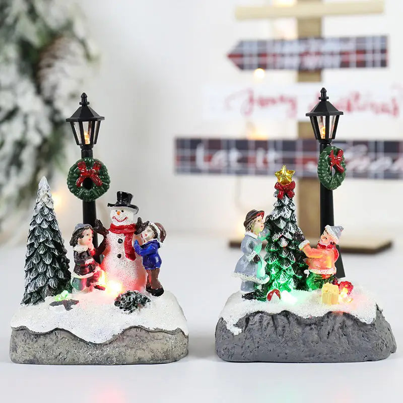 子どもたちが発光するライトで木を飾り付ける様子を表現した、LED雪だるまフィギュリンディスプレイを備えた、イルミネーションの施されたクリスマスハウスライトのミニチュア・ディオラマ2点。