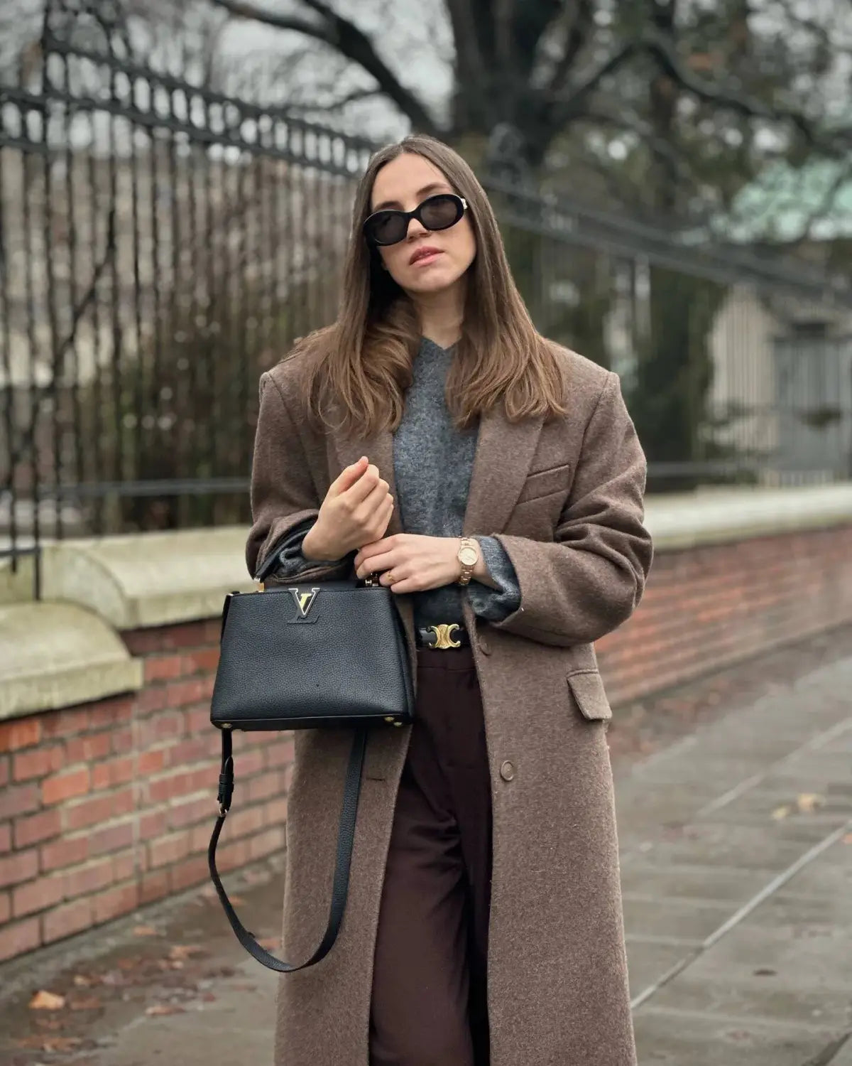 Black textured leather handbag with gold-tone LV logo and adjustable strap displayed with brown wool blend overcoat women winter commuter jacket.
