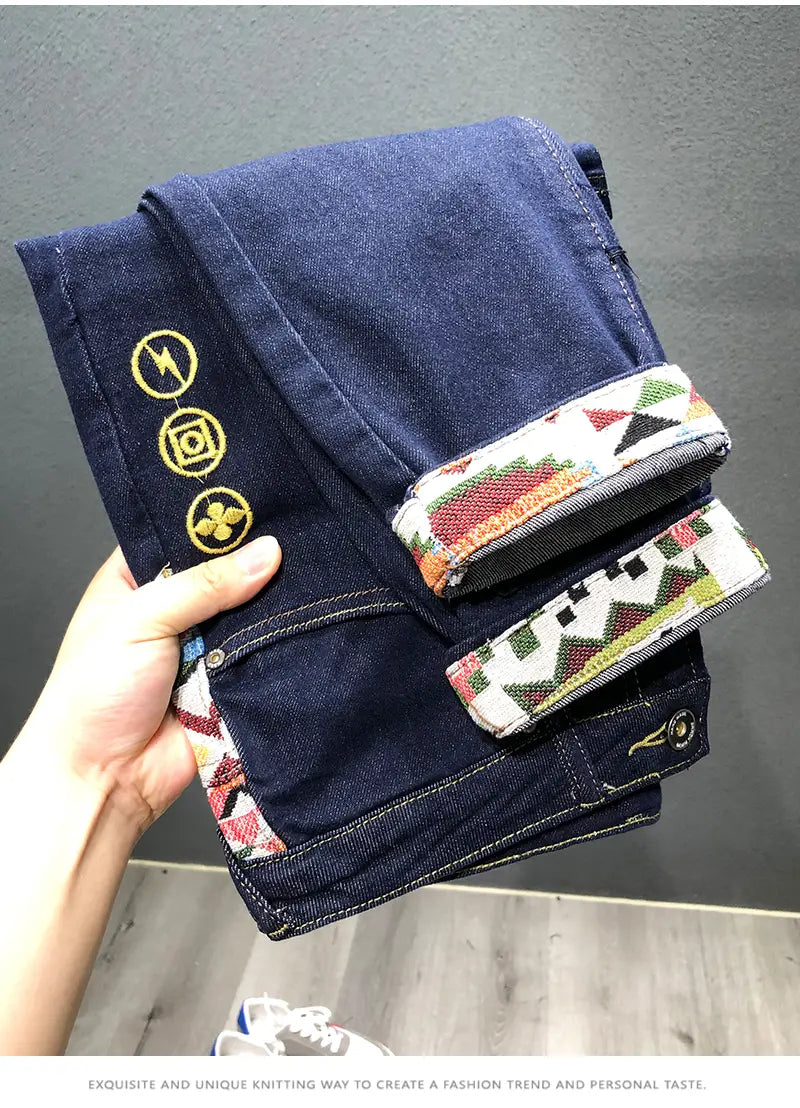 Men slim fit stretch white denim jeans with dark blue denim fabric embroidered with gold circular symbols on the leg and colorful geometric patterned cuffs.