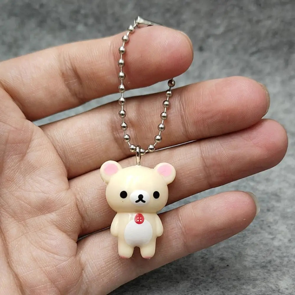 Cream-colored rilakkuma bear keychain with pink inner ears and a red button on its chest hanging from a silver ball chain as a cute DIY pendant.