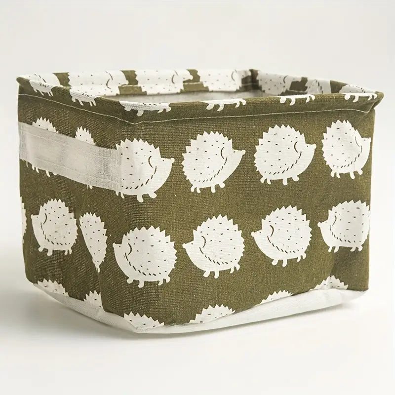 Panier de rangement pliable en tissu vert olive présentant un motif répété de hérissons blancs de style dessin animé avec des détails en points noirs, utilisé comme boîte de rangement décorative.