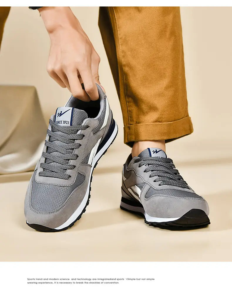 Herrenfreizeitsneaker in Grau und Weiß zum Gehen mit Mesh- und Wildleder-Obermaterial, schwarzen Gummisohlen und dezenten Branding-Details an der Zunge.