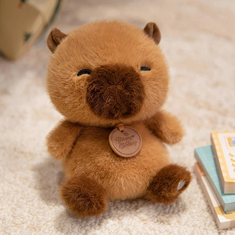 a soft plush brown capybara stuffed animal with a darker brown snout and ears wearing a round wooden tag that reads capybara gang from the sitting animals red panda fox sloth plush toys collection