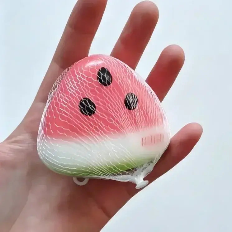 un jouet à mâcher et à malaxer en forme de fromage, pastèque, rose et vert, conçu pour soulager le stress, texture souple et molle, enfermé dans un sac à mailles transparent pour une apaisement efficace du stress lié au jouet.