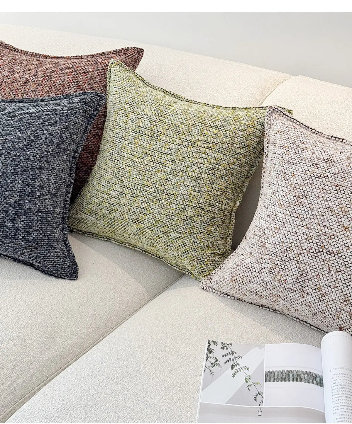 Quatre housses de coussin d’appoint en chenille dans des tons terreux atténués de rouge rouille, de gris anthracite, de vert olive et de beige, disposées sur un canapé de couleur claire, affichant leurs surfaces de coussin décoratif texturées.