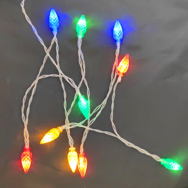 Eine Lichterkette aus RGB-LED-Weihnachts-Stringlights mit facettierten Glasglühbirnen, die in Rot, Grün, Blau und Gelb leuchten, auf einem weißen Kabel, ideal für festliche Raumdekoration.