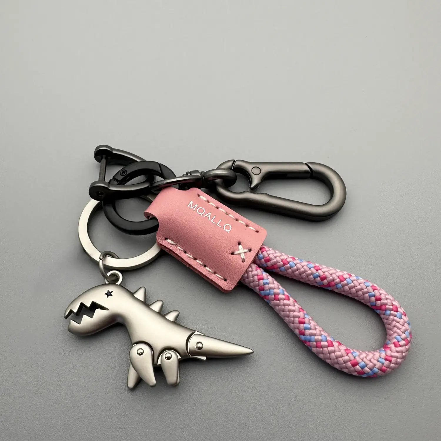llavero metálico con forma de dinosaurio color plata, con etiqueta de cuero rosa y correa de cuerda trenzada en un diseño de llavero de cuero con forma de dinosaurio trenzado.