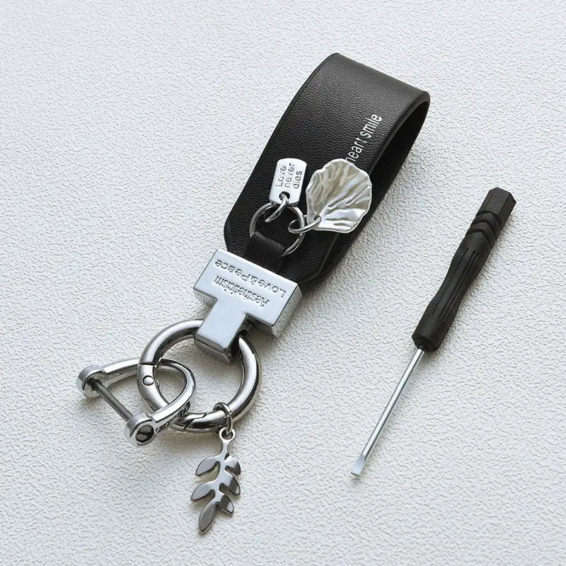 Llavero de piel negra con acentos metálicos plateados y dijes con forma de hoja, diseñado como un llavero de piel con funda en estilo francés para automóvil antirrobo.