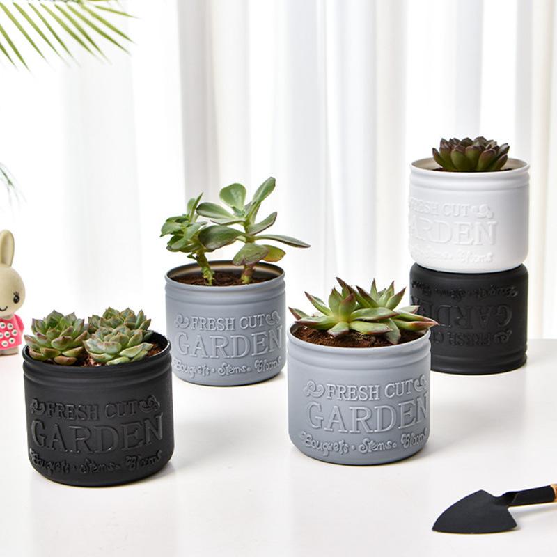 灰色および黒色の小型サイズのセラミック植木鉢。エンボス加工で「フレッシュカットのガーデンテキスト」が施され、室内用として小さな多肉植物をそれぞれ1株収容します。