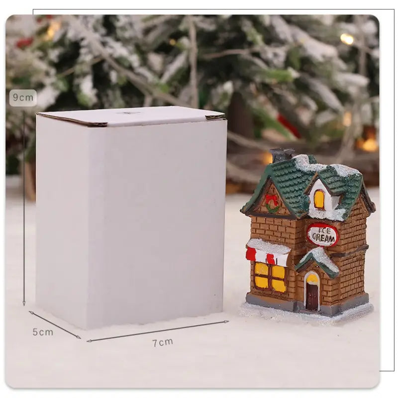Une boutique miniature de glace en briques brunes, avec un toit vert et des fenêtres éclairées en jaune, recouvertes de neige, comme veilleuse nocturne LED de maison de village de Noël alimentée par batterie.