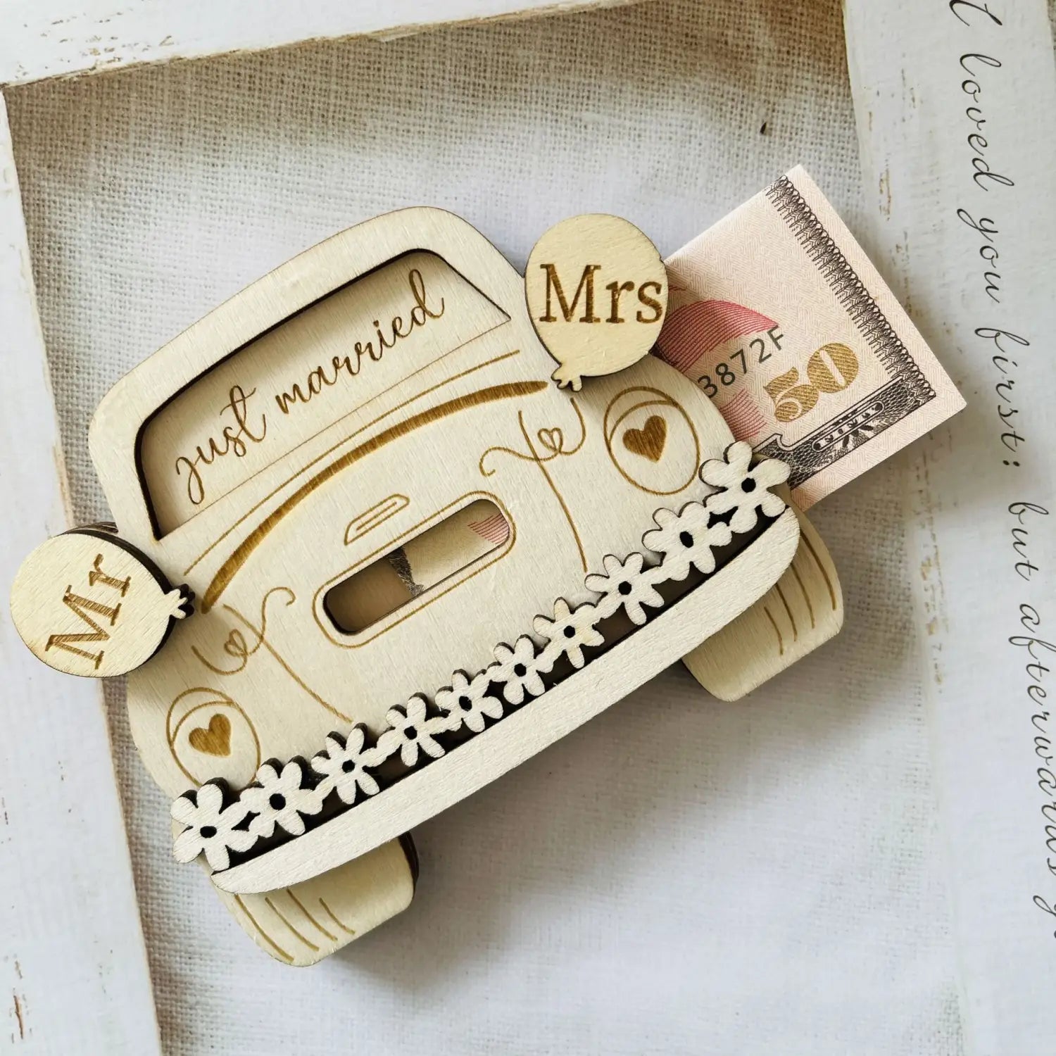 Eine hellfarbige hölzerne Geschenkbox für Geld zum Aufbewahren in Form eines Hochzeitswagens mit „Just married“ eingraviert auf der Windschutzscheibe und dekorativer Blumeneinfassung entlang der Seite