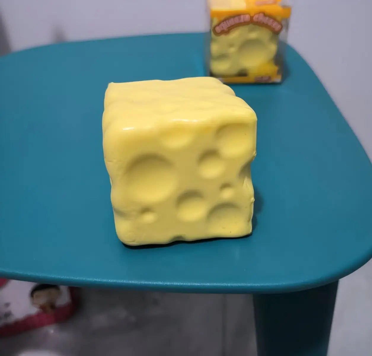 ein gelber, würfelförmiger Käsewürfel-Stressball mit glänzendem Kunststofffinish und charakteristischen Löchern, verwendet als knetbares Sinnes-Plaything