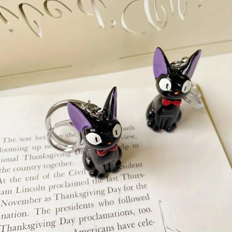 Black cat keychain made of cute pvc featuring purple ears and a red bow tie as a bag charm.