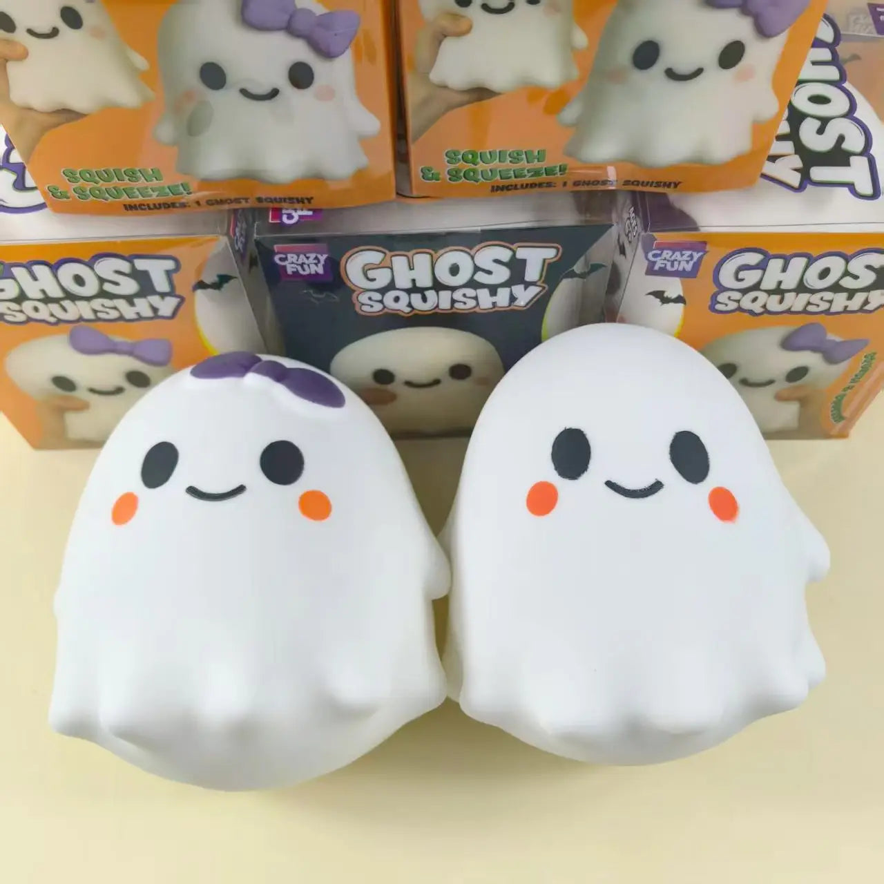 White ghost-shaped squishy slow rising stress relief toys with purple bows orange cheeks and a soft plush texture.