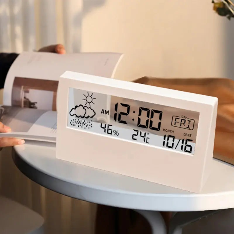 White rectangular digital weather desktop alarm clock displaying time date temperature and weather forecast on a sleek screen.