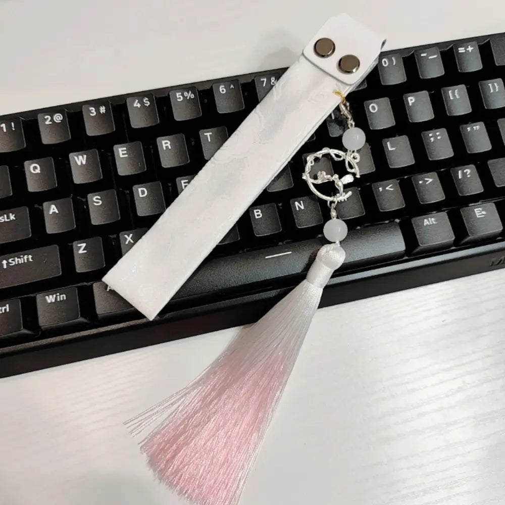 Marque-page en cuir blanc avec pompon argenté et perles décoratives, conçu comme une sangle personnalisée de type Ribbon Dragon pour clavier Wooting.