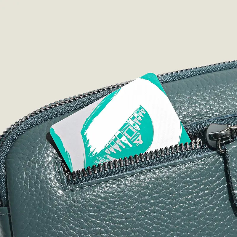 Eine Umhängetasche aus echtem, dunkelgrün strukturiertem Leder für Damen mit einer teal- und weißfarbenen Karte mit stilisiertem Grafikdesign, teilweise sichtbar aus der Öffnung des Reißverschlusses