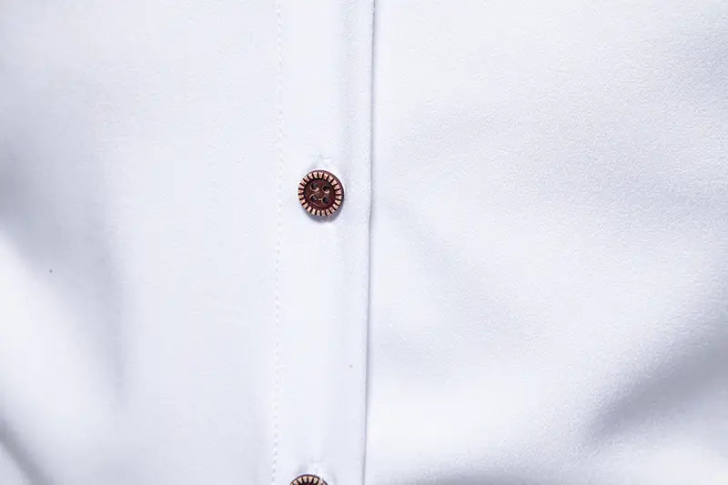 A round dark brown button with a sunburst pattern and metallic edges fastened on the front of a white men asymmetrical slant collar long sleeve casual shirt.