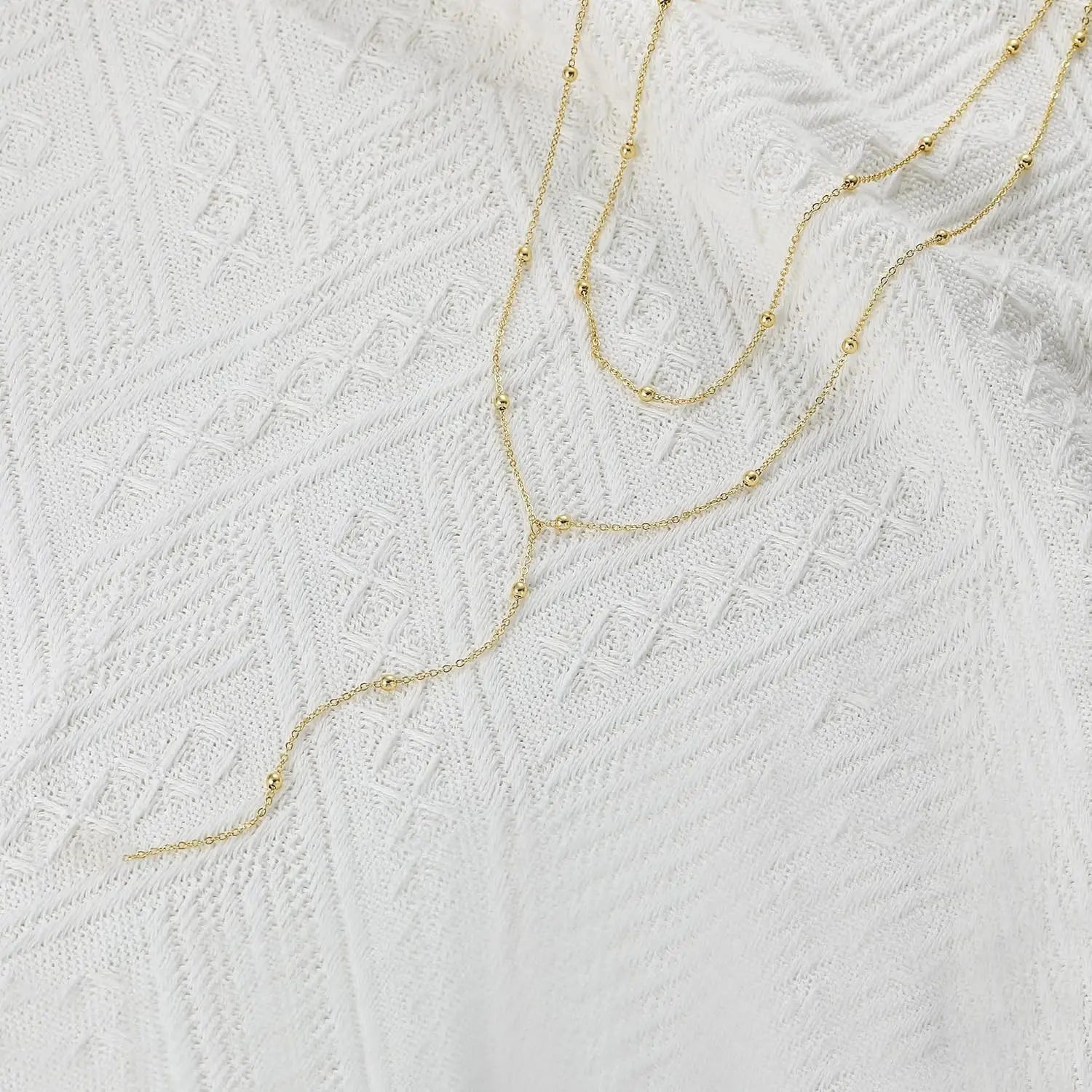 Un collier en « y » à superpositions délicates en or pour femmes, présentant des chaînes fines à tonalité or avec de petites perles sphériques.