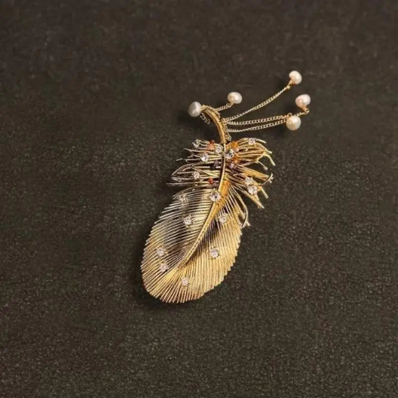 Broche à plume dorée délicate à pompon, ornée de diamants étincelants et de minuscules perles le long de sa tige.
