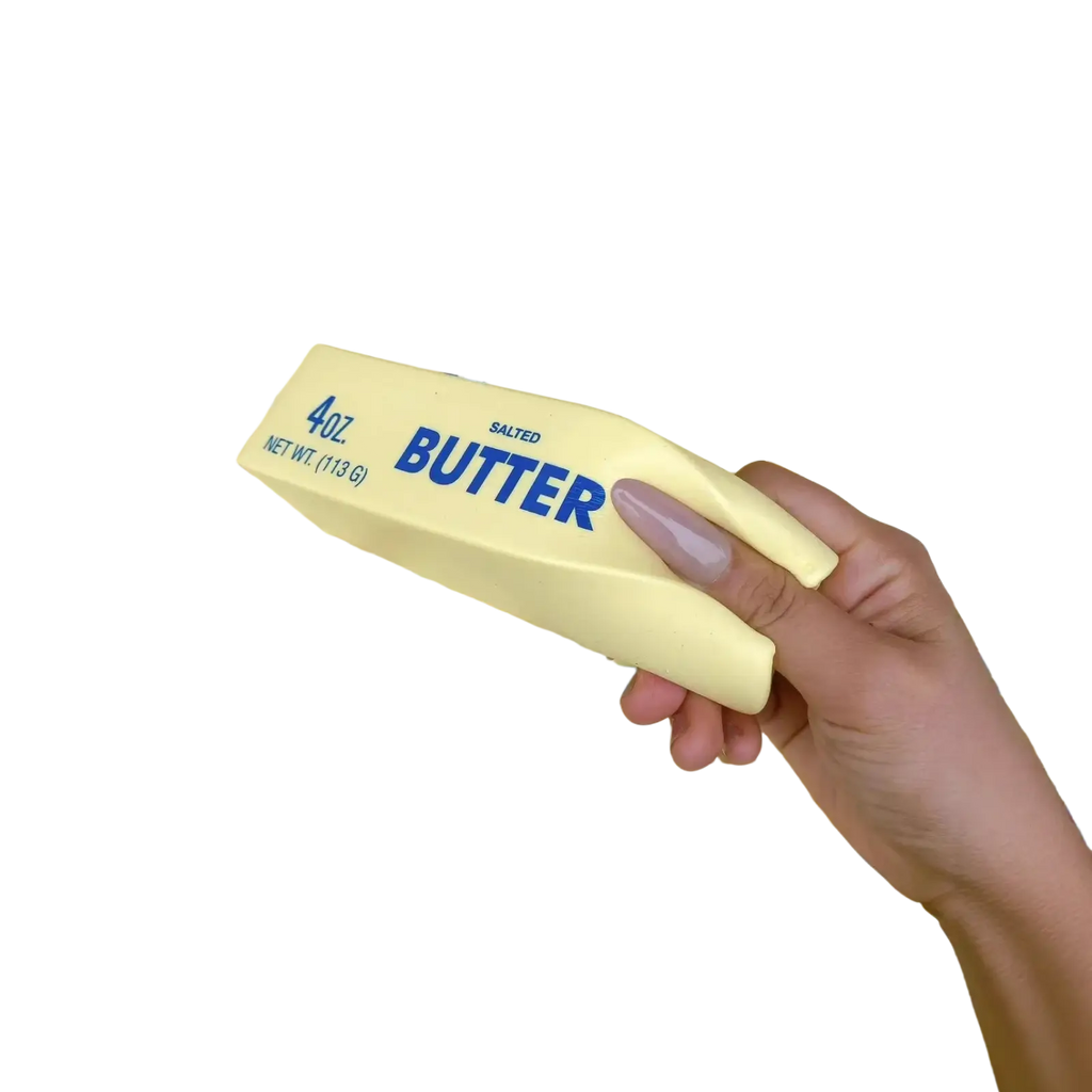 A hand holds a pale yellow 4oz salted butter stick wrapped in clear plastic as a soft slow rising squishy toy