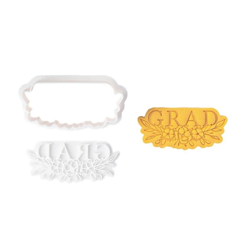 White plastic 2026 graduation cookie cutter set featuring a grad text and floral design alongside a yellow baked dough cutout with the same pattern.