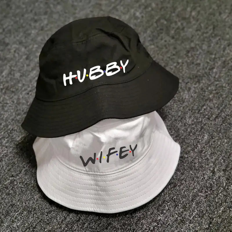 Chapeaux bob en coton noir et blanc avec « hubby » et « wifey » brodés dans une police ludique et colorée, inspirée de la série télévisée Friends, pour une utilisation lors d’un mariage.