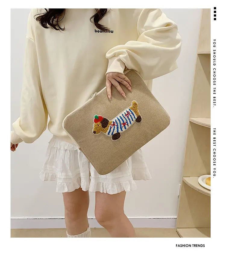 Beige Kord-Laptophülle für MacBook Pro mit gewebtem Clutch-Design, mit einer farbenfrohen bestickten Dackel-Figur, die eine rote Mütze und einen blau-weiß gestreiften Körper trägt.