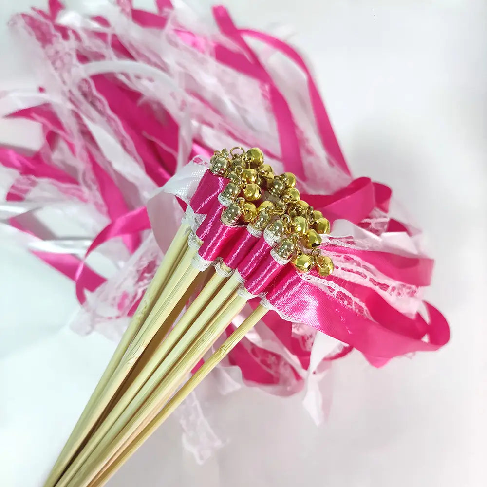 Baguette de ruban de mariage présentant un ruban en satin rose noué avec de la dentelle et des cloches dorées en partie supérieure.