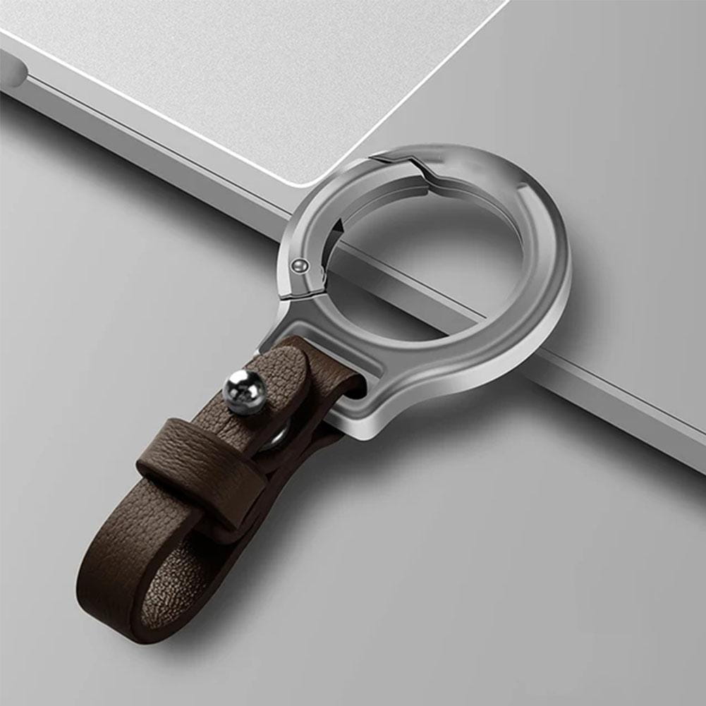 小さな銀色のボタンが付いた茶色のレザーストラップを備える銀色の金属製ラップトップスタンド。金属クリップおよびリング付きのレザー製カ―キーケースと組み合わされている。