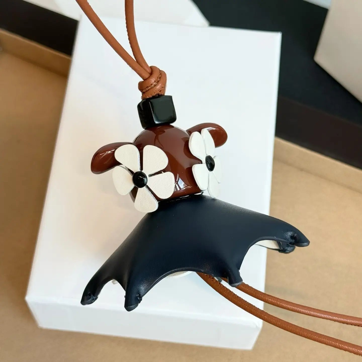 Llavero colgante con forma de mantarraya de cuero marrón y negro, con acentos de flor blanca, diseñado como un tierno encanto de bolso de diseñador.