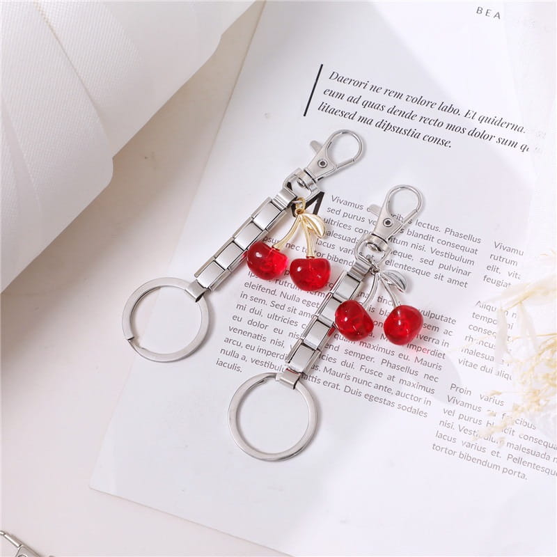 Llavero con dije de eslabones italianos de metal en tono plata, con dos dijes de cereza roja y un pequeño lazo dorado para uso personalizado en bricolaje.