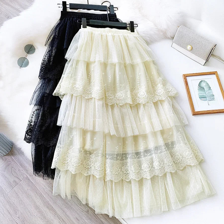 Jupe longue évasée en ligne A à taille haute de couleur crème, confectionnée en tulle à volants superposés, avec une bordure en dentelle délicate et une broderie florale.
