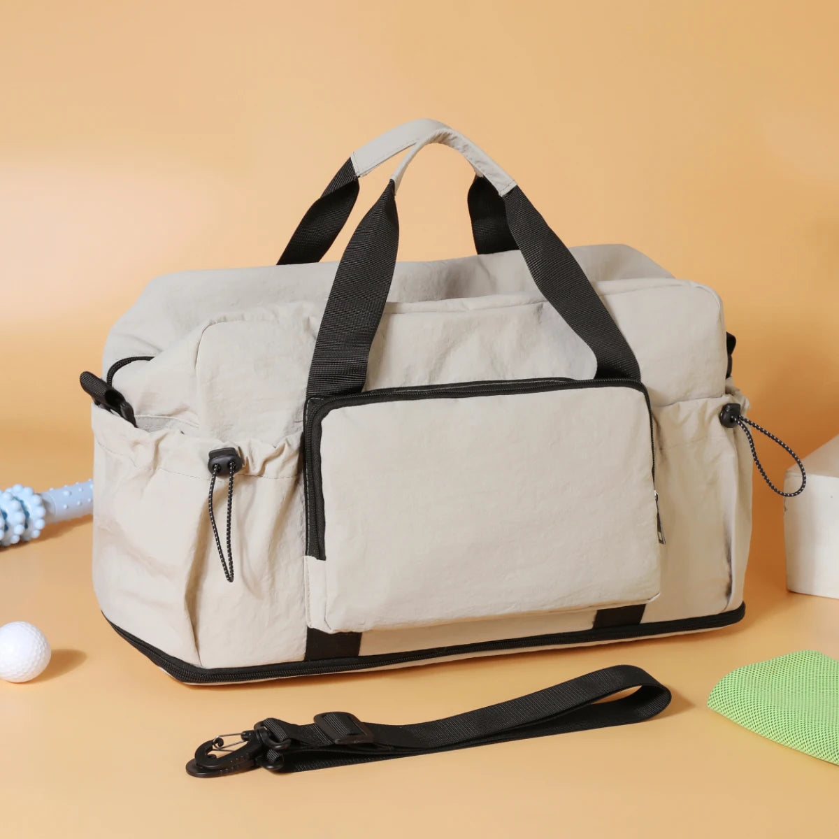 Sac de voyage duffel beige et noir en matériau léger, doté de poignées renforcées, de poches latérales et d’une bandoulière amovible pour une utilisation en bagagerie extensible.