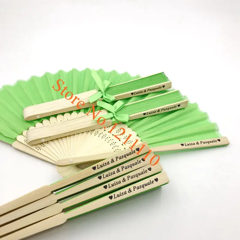 Light green and natural wood custom wedding hand fans made of bamboo and silk with personalized engraved luisa and pasquale text and heart symbols on the handles.