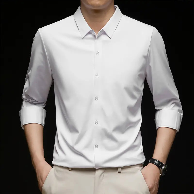 Una camisa de vestir para hombre sin arrugas blanca e impecable, confeccionada con tejido suave, que presenta un cuello clásico y parte delantera abotonada.