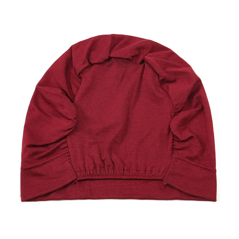 A soft deep red stretchy knit beanie with a gathered elastic band at the bottom from the stretchy jersey hijab cap and turban set.