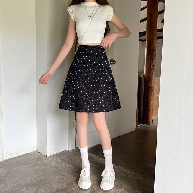 Falda midi línea A negra con lunares blancos y cintura alta mostrada desde el frente en un producto titulado falda midi línea A roja con lunares.