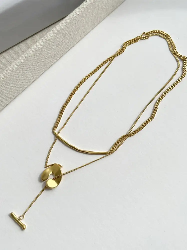 Collier pendentif à superposition géométrique doré pour femmes, présentant des maillons de chaîne aux tons dorés et des pendentifs géométriques abstraits.