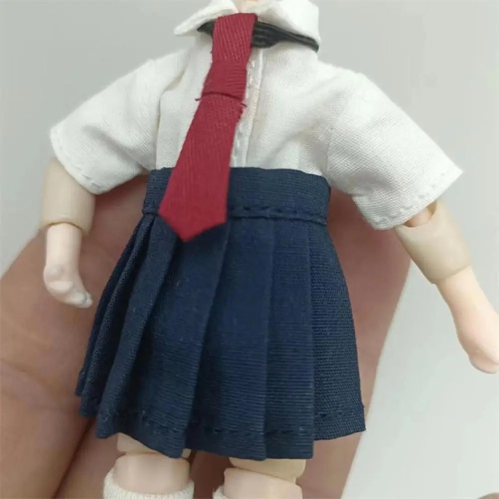 白い半袖シャツ、紺色のプリーツスカート、赤いネクタイのスクール衣装を身に着けたミニチュアのOb11ドール。