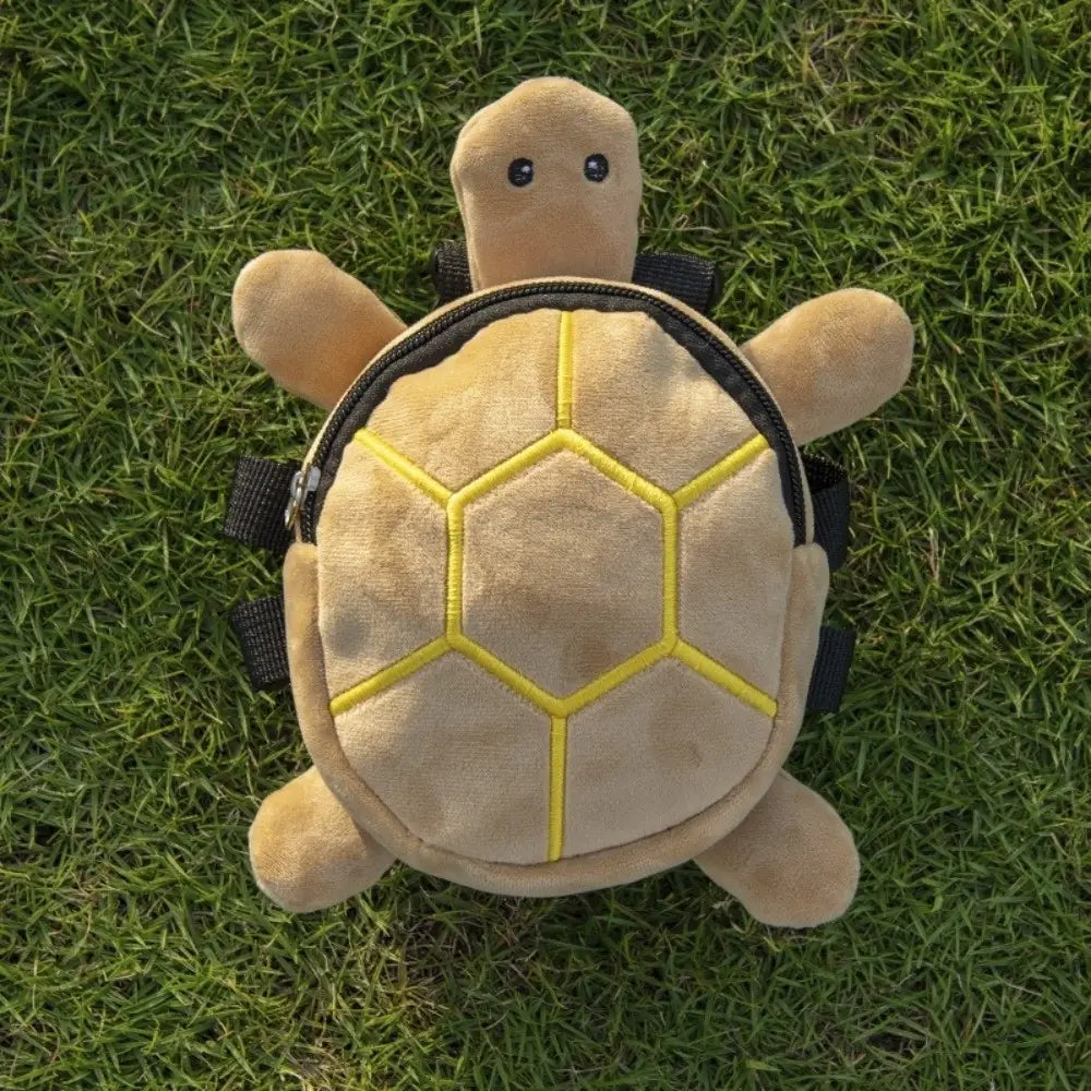 A plush tan turtle shape dog backpack with yellow stitched hexagonal patterns on its shell and black straps designed as a pet carrier.