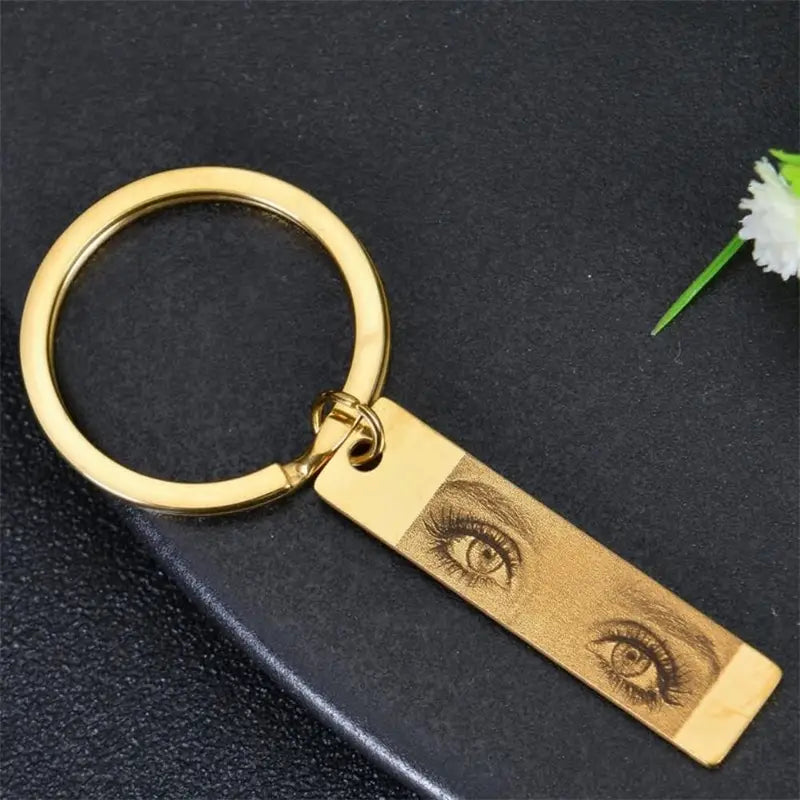 Gold-colored metal custom eye photo engraved stainless steel keychain with a rectangular tag featuring a detailed illustration of two eyes.