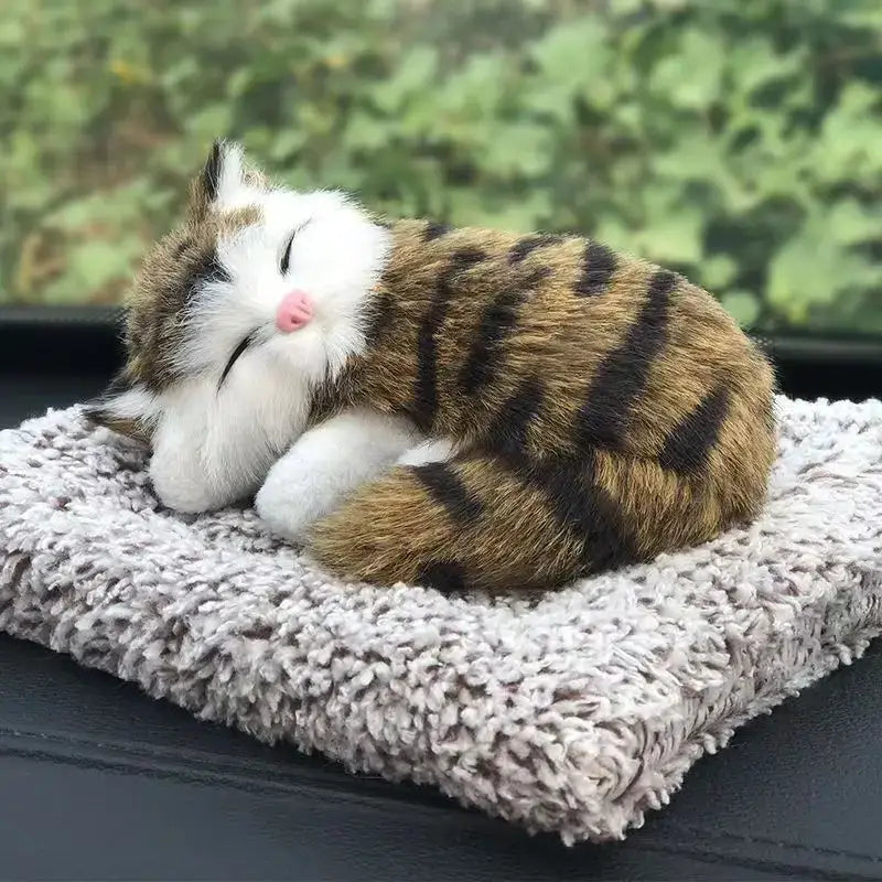 A simulated sleeping cat plush toy with sound features a brown and black striped tabby design with white fur on its face and paws and a pink nose resting on a textured gray cushion.